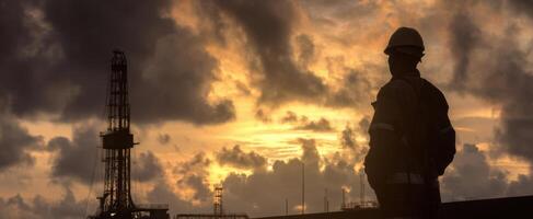 The silhouette of a worker overlooking an oil drilling site at sunset photo