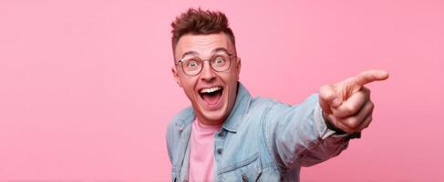 The cheerful young man joyfully pointing at something exciting in a pink setting. photo