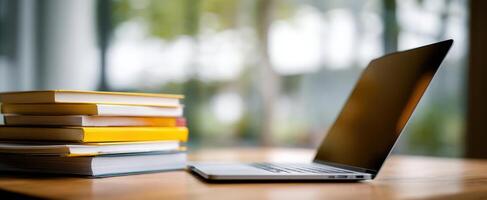 The sleek laptop placed beside a stack of colorful books on a wooden desk. photo