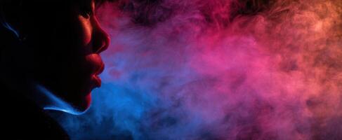 The silhouetted profile exhaling vapor amidst colorful smoke in a dramatic setting. photo