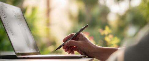 The modern workspace featuring a hand writing on a laptop in nature. photo