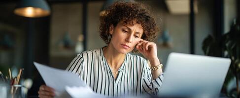 The woman thoughtfully analyzes documents while seated at her modern office workspace. photo