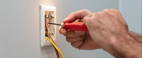 The electrician performing repairs on electrical wiring with a screwdriver. photo