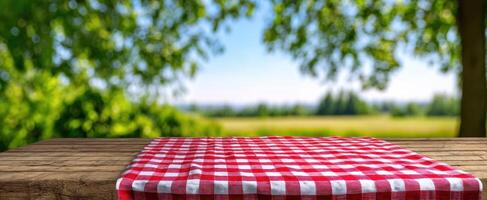 The red checkered picnic blanket on a rustic wooden table in a lush outdoor setting. photo