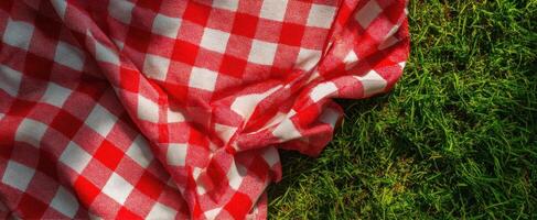 The vibrant red checkered picnic blanket resting on lush green grass photo