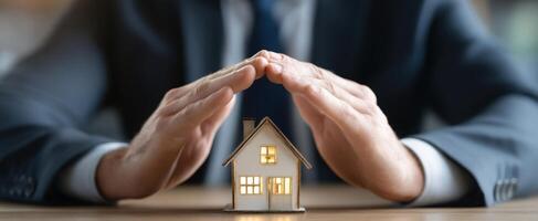 The miniature house protected by hands representing home insurance and security. photo