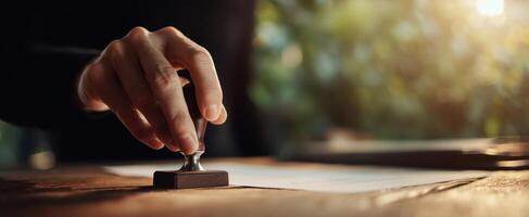 The hand applying a seal stamp over important documents on a wooden desk. photo