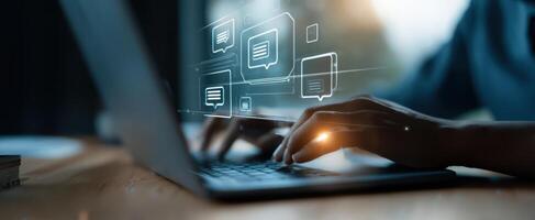 The hands typing on a laptop surrounded by digital communication icons. photo