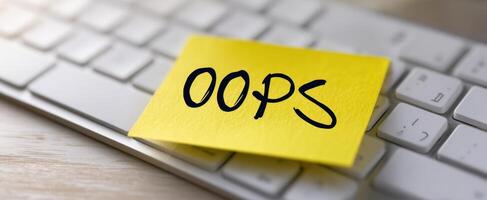 The bright sticky note stating 'Oops' on a computer keyboard. photo