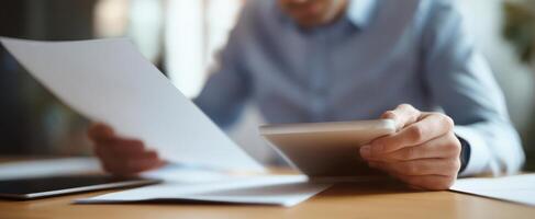 The professional examining documents while using a tablet in a modern workspace. photo