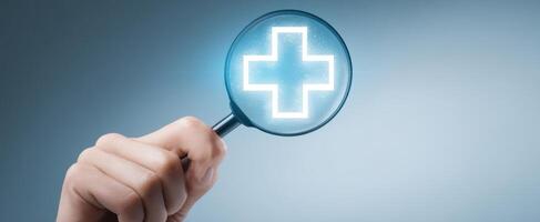 The hand holding a magnifying glass over a glowing medical cross symbol photo