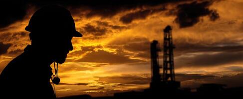 The silhouette of a worker against a vibrant sunset in an industrial setting. photo