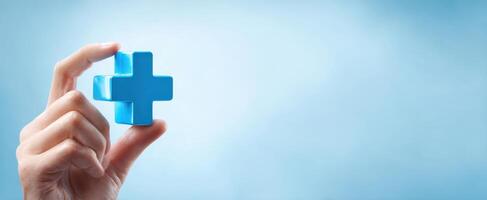 The hand holding a blue plus symbol representing health and wellness. photo