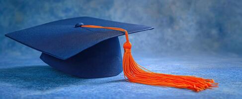 The graduation cap with an orange tassel on a textured blue background. photo