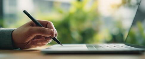 The hand writing on a laptop in a modern workspace surrounded by greenery. photo