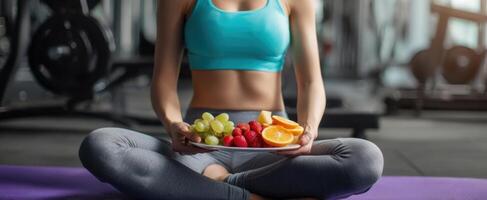 The woman enjoying a colorful plate of fresh fruits in a gym setting. photo
