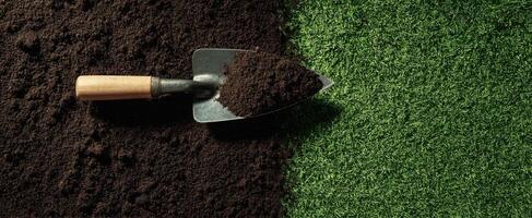 The shovel rests on dark soil beside vibrant green grass. photo