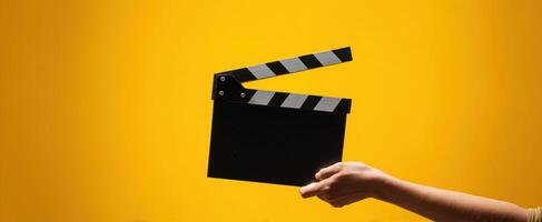 The hand holding a classic clapperboard against a bright yellow background. photo
