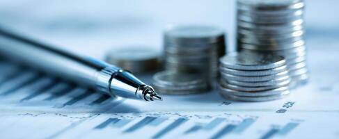 The pen resting on a stack of coins and financial data sheets. photo