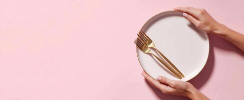 The elegant hands holding a plate with golden forks on a pink background. photo