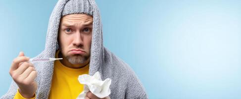The sick man with a thermometer under a blanket looking worried and uncomfortable. photo