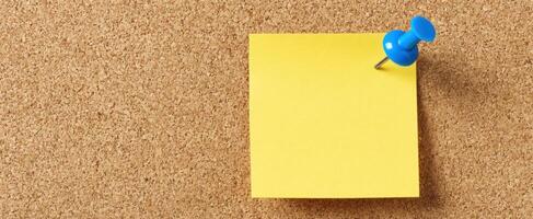 The yellow sticky note pinned on a corkboard background for reminders. photo