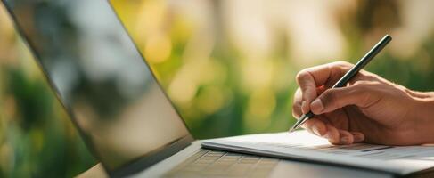 The hand writing notes beside a laptop in a relaxed, outdoor workspace. photo