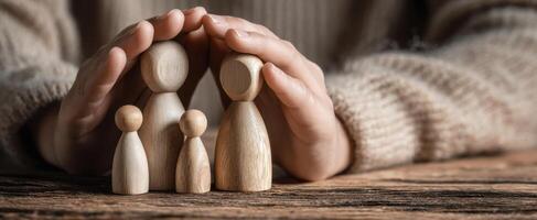 The wooden family figures protected by nurturing hands on a wooden surface photo
