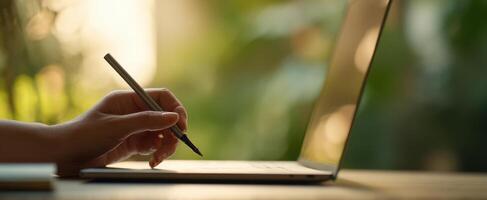 The hand writing on a laptop in a bright, natural workspace setting. photo