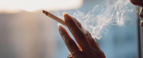 The hand holding a cigarette exhaling delicate wisps of smoke during sunset photo