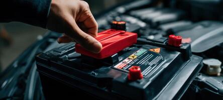 The hand installing a red battery cover in a car engine compartment. photo