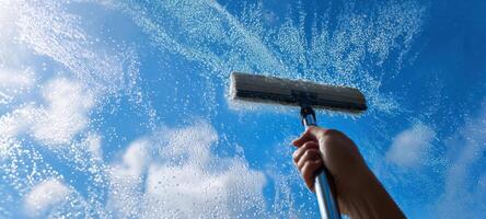 The hand using a squeegee to clean a window against a bright sky photo