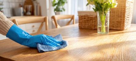 The person cleaning a wooden table with a blue cloth in a bright kitchen. photo