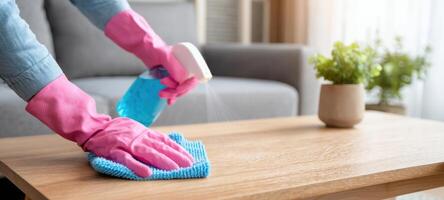 The woman cleaning a wooden table with blue cloth and pink gloves photo