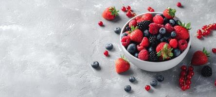 The vibrant bowl of mixed berries on a rustic gray surface. photo