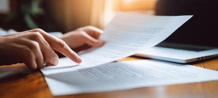 The hands reviewing important documents beside a laptop in a bright workspace. photo