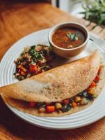 Savory crepe filled with mixed vegetables served with soup and a side salad on a white plate. photo