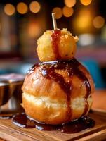 Close up of a delicious glazed donut topped with a fried potato ball and drizzled with gravy. photo
