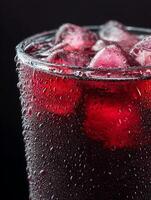 Close up of a glass of refreshing red beverage with ice cubes and condensation. photo