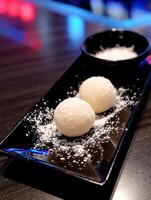 Close up of Two Mochi Balls on a Black Plate with Powdered Sugar. photo