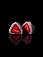 Close up of two halves of a strawberry mochi dessert, showing the vibrant red fruit inside against a black background. photo