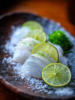Close up of fresh fish sashimi with lime slices and sea salt on a rustic plate. photo