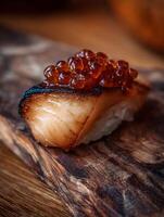 Close up of grilled sushi topped with orange caviar on a wooden board. photo