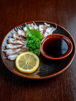 Sliced Squid Dish with Lemon and Soy Sauce on Dark Plate. A close up shot of a delicious seafood appetizer. photo
