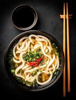 Delicious Udon Noodle Soup in a Dark Bowl with Chopsticks and Soy Sauce. photo