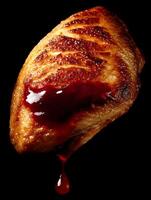 Close up of grilled chicken breast with red sauce dripping down, isolated on black background. photo