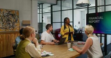 A group of young people are sitting at a table in an office meeting. A woman submits a financial report. video