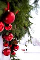 The photo features a diminutive Christmas tree adorned with red ribbons in a silver pail, resting on a red surface, with a blurred background of a light-colored wooden fence.