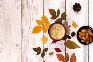 Overhead shot of an autumn-themed arrangement with a white coffee cup and saucer as the central element, complemented by fallen leaves, acorns, and a delicate floral accent. photo