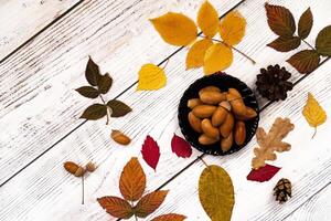 A simple and elegant flat lay depicting a coffee cup, saucer, autumn leaves, acorns, a candle, and a flower, all neatly arranged on a light wooden background. photo